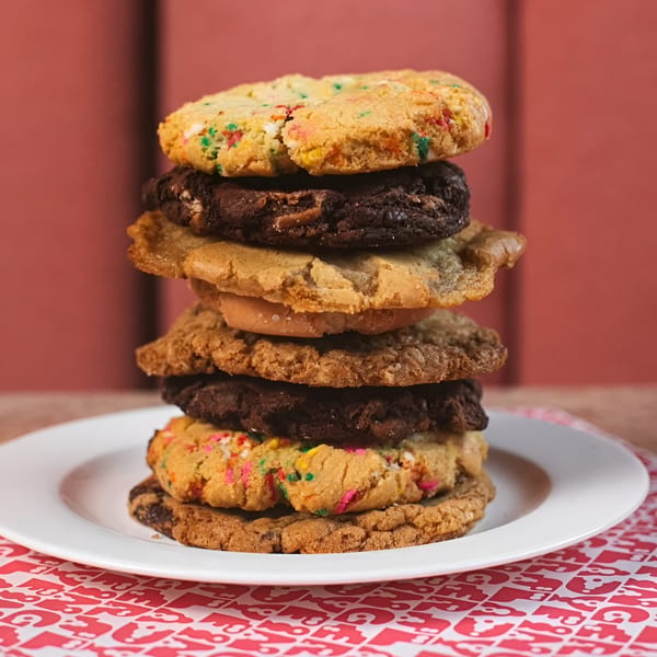 A tall stack of assorted Ladyfingers Bakery + Bar cookies on a white plate with a red background.
