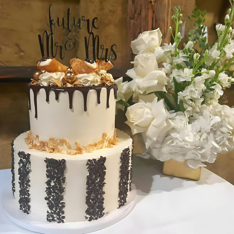 Two-tier white wedding cake with chocolate drip, cannolis, and a "Future Mr & Mrs" topper.