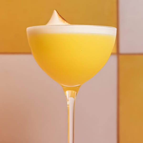 A vibrant yellow cocktail with a white foam topping and a toasted meringue garnish.