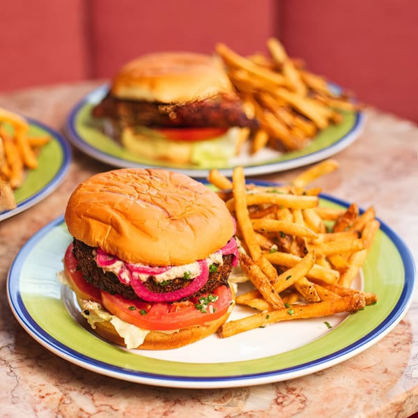 Two burgers with fries on colorful plates, featuring pickled onions and fresh tomatoes.