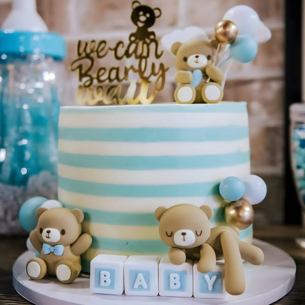 A baby shower cake with blue and white stripes, teddy bears, and "BABY" blocks.