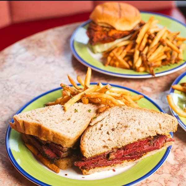 Two plates of sandwiches and french fries on a marble table at Ladyfingers Bakery + Bar.