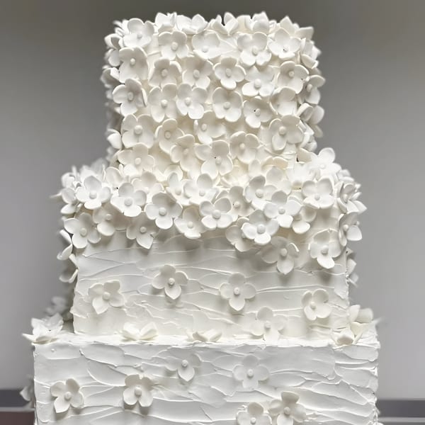 A three-tiered white wedding cake from Ladyfingers Bakery + Bar, adorned with delicate white sugar flowers.
