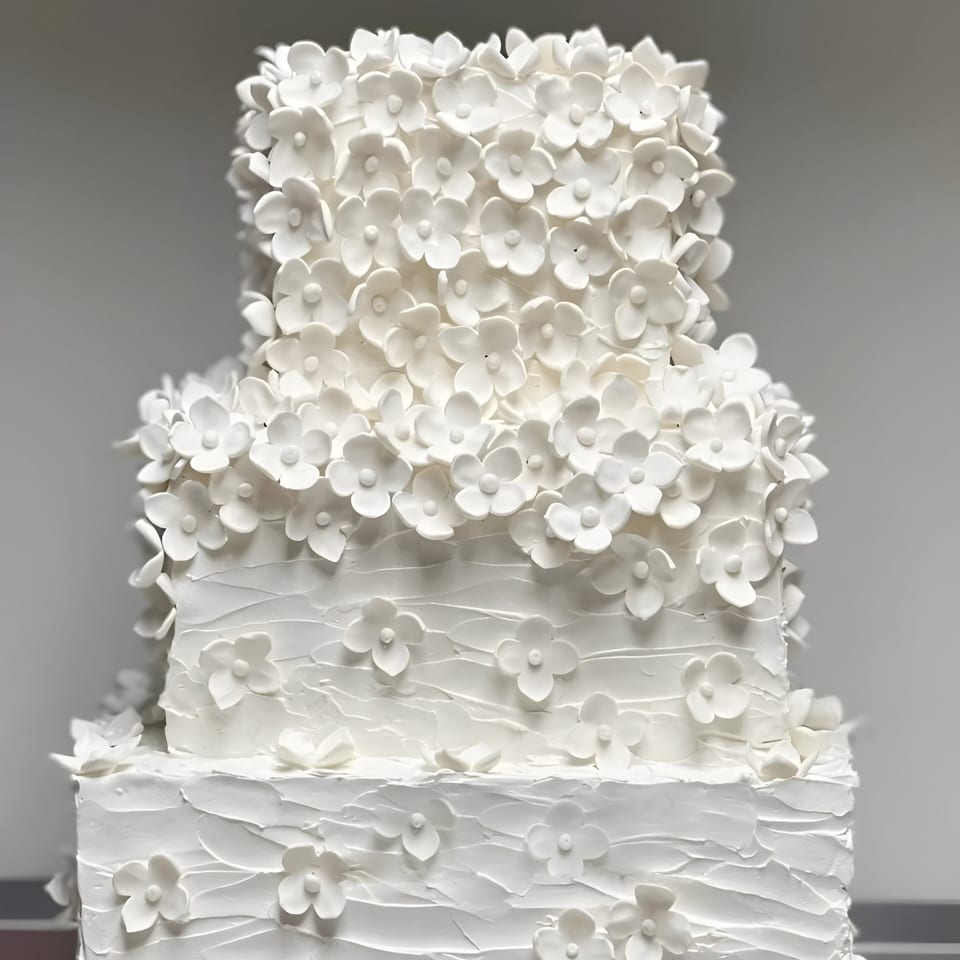 A three-tiered white wedding cake from Ladyfingers Bakery + Bar, adorned with delicate white sugar flowers.